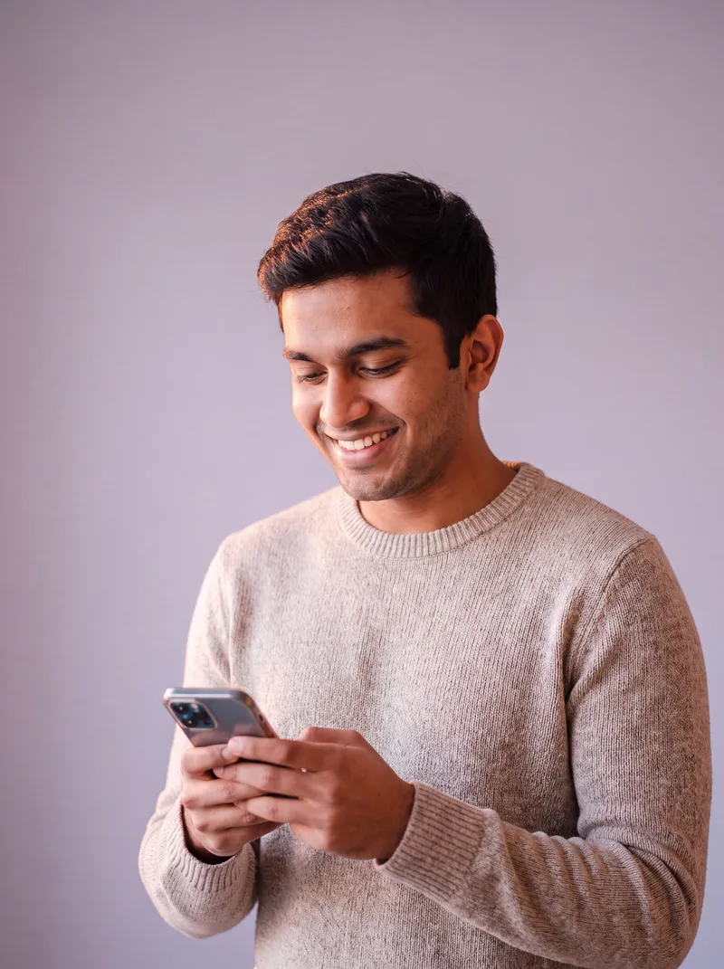 A young man smiling at his phone.